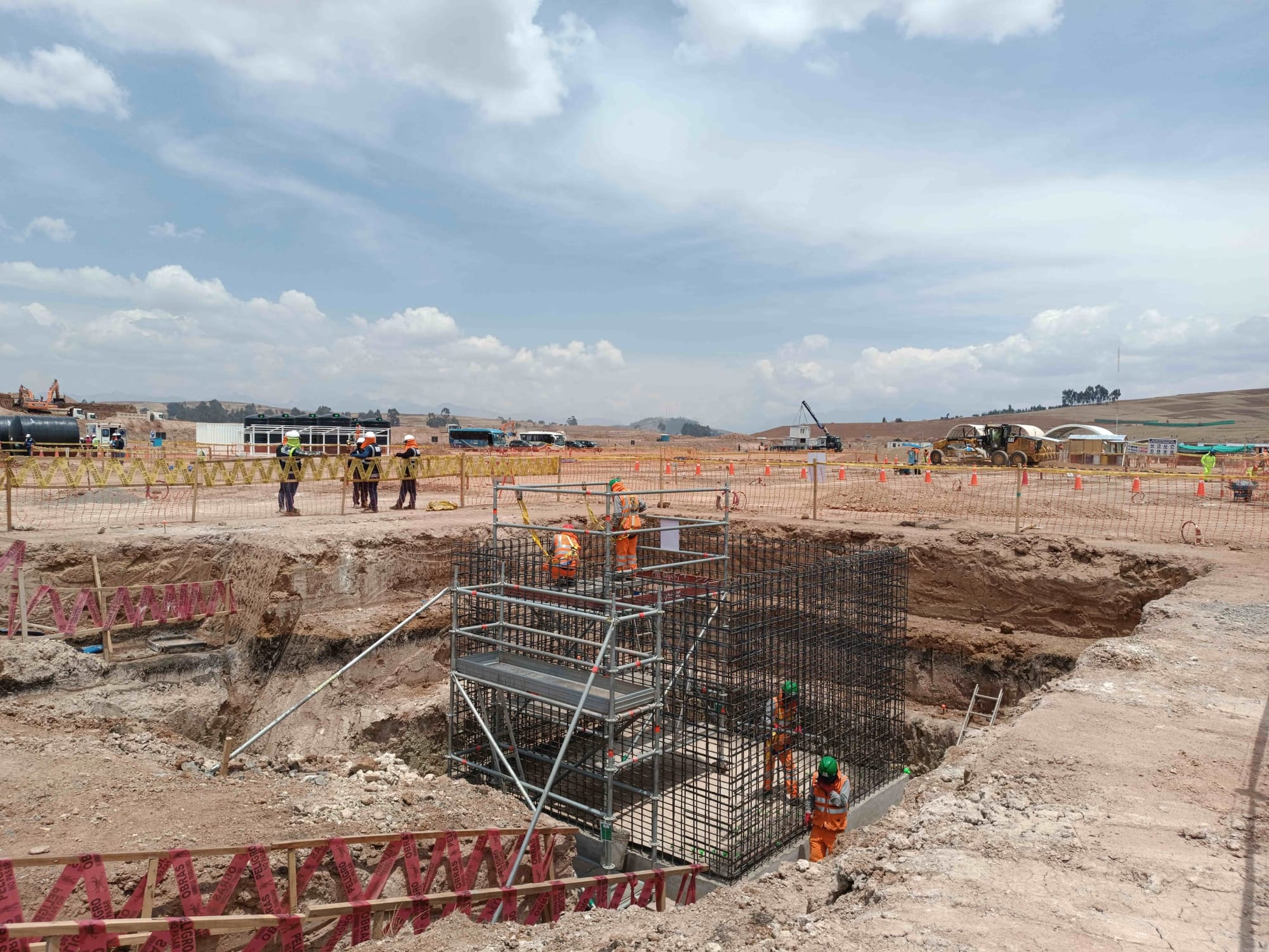 Vista panorámica de una obra aeroportuaria con excavación, acero de refuerzo, andamios, trabajadores y maquinaria